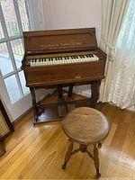 Front view of the entire Estey organ with foot pedals and wooden adjustable swivel seat, showing the wooden body and pedal platform.