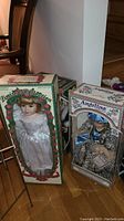 Two boxed vintage porcelain dolls side by side on floor, one in white satin dress, the other in leopard print outfit.