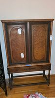 Full view of vintage wooden cabinet showing two paneled doors, single drawer, and turned legs with stretcher base.