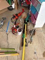Full view of all yard tools arranged on the ground including string trimmer, cultivator, shovels, rake, pole saw, sprinkler and clippers.