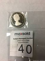 Photo of 1983 Proof Dollar coin obverse featuring Queen Elizabeth II in protective plastic sleeve alongside auction lot label.