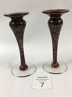 Pair of brown and red swirled hand blown glass candlesticks with clear round bases photographed against a white background.