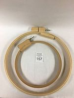 Two extra wide embroidery hoops, one smaller and one larger, stacked on a white surface showing steel wing nuts and hardwood frames.