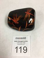 Dragonflies and leaf design on a polished black stone scroll weight, shown from one angle.