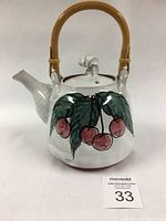 Front view of Elaine Hughes-Games studio teapot with cherry motif and bamboo handle against white background.