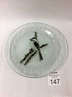 Top-down view of the round clear glass plate showing the detailed fused bird and branch design in the center.
