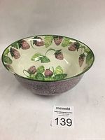 Front angled view of the bowl showing the interior strawberry and leaf design and speckled exterior glaze.