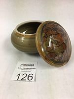 Small round lidded porcelain box with multicolored lid showing iron glaze and celadon ceramic body.