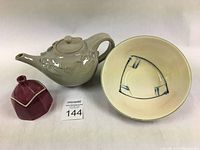 White celadon-glazed teapot with 3D wave design, red earthenware bowl with cream glaze and oxide decoration, and maroon-glazed octagonal clay box shown together.
