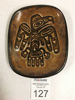 Top view of a rectangular red clay dish with rounded edges and a carved stylized raven design in Haida style.