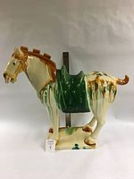 Front-left angle view of large SAN CAI style ceramic horse sculpture showing white and butterscotch glossy glaze with green saddle detail on rectangular base.
