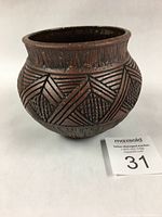 Front angled view showing incised geometric designs in black on brown wash pottery pot with flared rim.