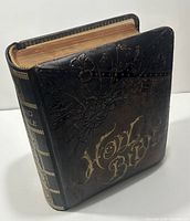 View of closed Bible showing black leather cover with embossed floral pattern and gold gilded text on spine and front cover.