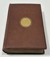 View of book closed showing brown cover with a gilded circular emblem depicting two figures and palm tree with inscription.