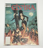Front cover showing comic book style illustration of Elvira standing on a tree stump with a crowd and haunted house in the background.