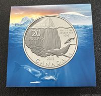 Silver coin with iceberg and whale design on a card backing depicting an oceanic scene with iceberg and whale underwater.