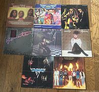 Eight vinyl albums laid out on wood floor, showing front covers visible with all albums identifiable by title and artwork. Includes Lynyrd Skynyrd, REO Speedwagon, Three Dog Night, Pat Benatar, Van Halen.