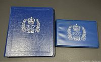 Two blue albums with silver embossed '1977 The Queen's Silver Jubilee' on covers; one larger binder style and one smaller booklet style.
