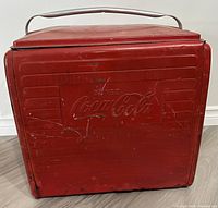 Front view of red metal Coca-Cola cooler showing embossed 'BUVEZ Coca-Cola' logo and visible age wear including scratches and paint loss.