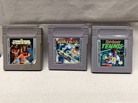 Photo showing the three Nintendo Game Boy cartridges: WWF Superstars, Alleyway, Top Rank Tennis, arranged side by side on a light-colored surface.