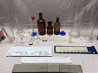 Full view of chemistry lot including various glassware, reagent bottles, small beakers, and slide rules spread out on a table.