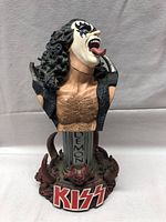 Front view of Gene Simmons KISS bust statue showing detailed face paint, tongue, chest hair, and decorative base with KISS logo.