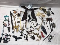 Overview of assorted fantasy figurines and accessories on white cloth background, showing various weapons, wings, limbs, and figurines of humanoid and creature types.