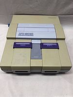 Front view of the beige Super Nintendo console with the cartridge slot cover closed and purple power and reset buttons visible.