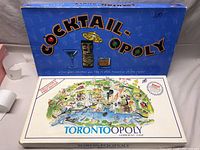 Photo of the Cocktail-opoly and Torontoopoly game boxes showing artwork and branding.