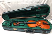 Violin in open hard case with green velvet lining, bow placed in a compartment.