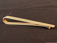 Side view of the polished 14k gold tie bar on black background