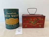 Front view of Christie's Cheese Wafers biscuit tin and Union Leader Cut Plug tobacco tin side by side showing labels and overall condition.