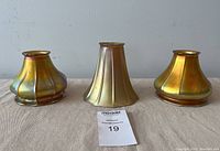 Three iridescent gold lamp shades arranged side by side on fabric surface