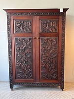 Front view of walnut wardrobe with two carved doors, floral relief panels, brass knobs, and carved border
