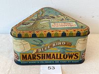 Front view of triangular Blue Bird Marshmallows tin showing logo, decorative birds, marshmallow images, and company name.