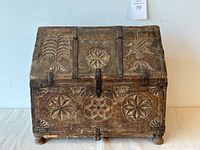 Full front view of carved wooden chest showing overall form, carvings, hinged lid, latch and feet