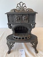 Front view of small cast iron wood stove showing floral doors, footrest, ornate legs and top vent