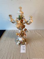Full view of antique porcelain candelabra with five arms, showing Cupid figures at the base and colorful floral detailing.