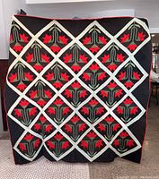 Front view of full quilt showing black background and repeating red and green appliqué floral blocks