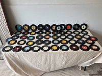 Wide view of over 50 vinyl 45 RPM records laid out on table showing front label variety and quantity.