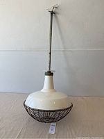 Front view of the white porcelain industrial pendant light with protective wire cage below showing overall shape and hanging rod with exposed wiring.