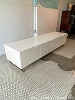 Front left angle view of high gloss white credenza on polished steel legs