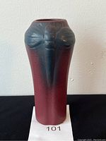 Front view of plum colored vase with raised green dragonfly motif on black background