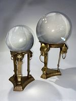 Pair of crystal balls with brass lion head stands, showing full front and side views with detail on lion heads and rings.
