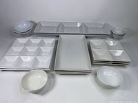 Wide shot showing all trays and bowls arrayed together, white ceramic glossy finish, various compartment configurations.