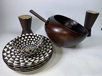 Set of 2 wooden pillars with brass tops, 1 large wooden bowl with handle, 10 black and white triangle patterned plates, and 1 matching bowl.