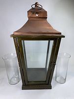 Front view of the glass and wood candle lantern flanked by two clear glass candle holders