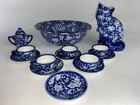 Blue and white ceramic tea set includes five cups with saucers, sugar pot with lid, large bowl, and cat figurine, all featuring floral pattern.