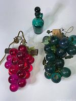 Overview photo of all three items: red glass grape lamp, green glass grapes decor, and green glass decanter.