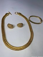 Photo showing the gold-tone chunky necklace, matching clip-on earrings and wide bangle bracelet aligned on a neutral white background.